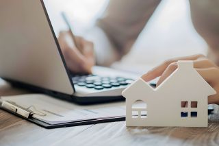 Foto: Person bearbeitet Akten, Modell eines Hauses im Vordergrund